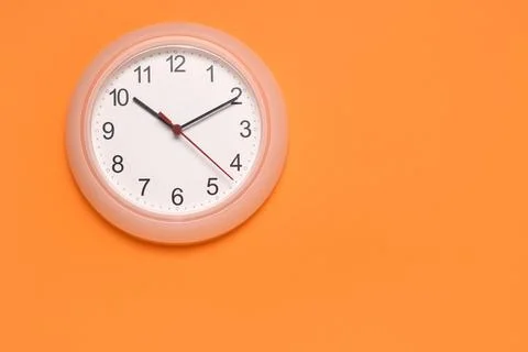 Wall clock on orange background showing time Stock Photos