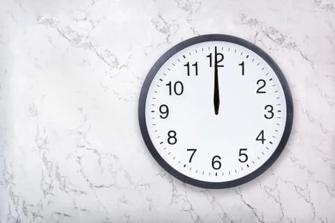 Wall clock show the twelve o'clock on white marble texture. Office clock show Stock Photos