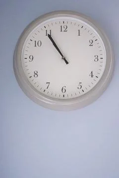Wall clock showing time almost eleven o'clock on a light blue background. C.. Stock Photos