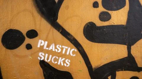 Wall graffiti featuring "plastic sucks" in white and slogan on golden background Stock Photos