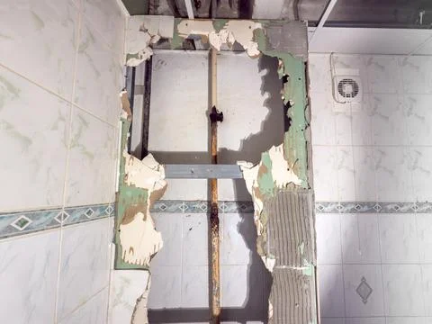 The wall has damage, with an exposed rusty water pipe and crumbling tiles Stock Photos