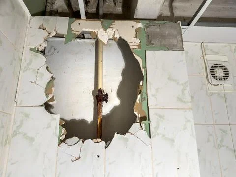The wall has damage, with an exposed rusty water pipe and crumbling tiles Stock Photos