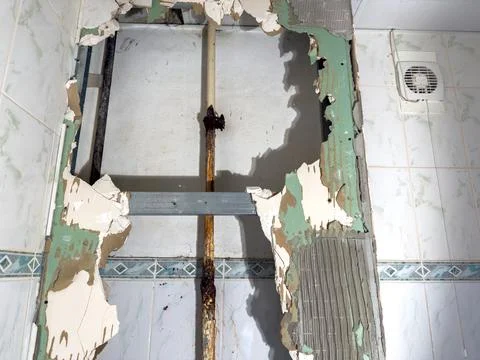 The wall has damage, with an exposed rusty water pipe and crumbling tiles Stock Photos