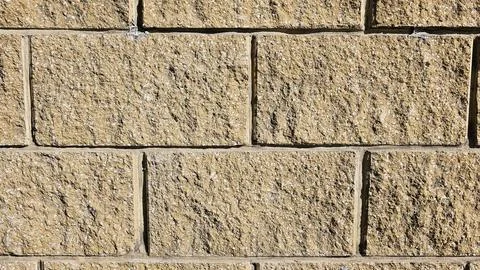 The wall is made of decorative rectangular light brown stone. Stone background Stock Photos