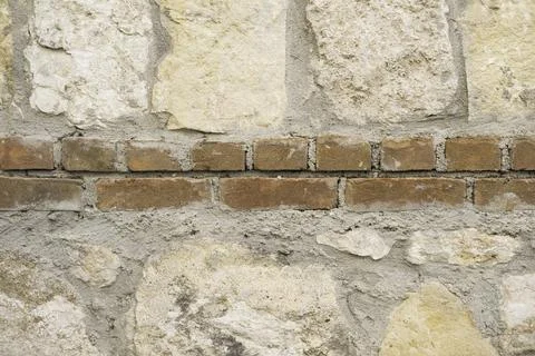 A wall made of large light limestone stones and a strip of red bricks Stock Photos