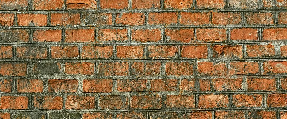 The wall is made of old orange bricks, the masonry is uneven. Stock Photos