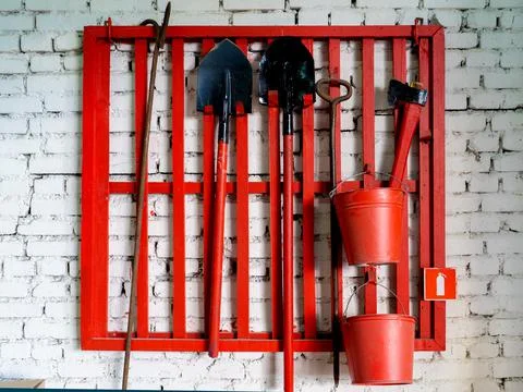 Wall-mounted fire shield with fire-fighting tools. Shovel, hook , axe, cone b Stock Photos