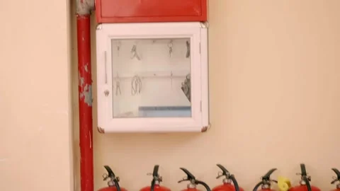 A wall-mounted red fire hose reel cabinet and fire extinguishers Stock Footage 340564897