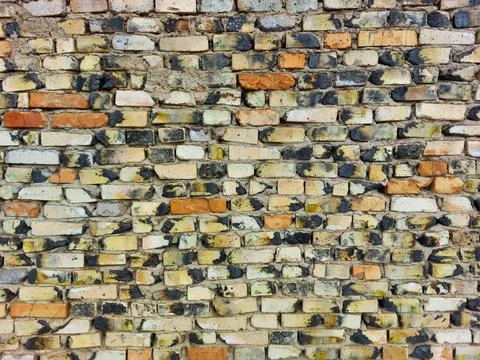 Wall of old baked bricks red brown white yellow black, gray uneven rows close-up Stock Photos