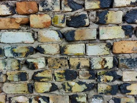 Wall of old burnt bricks of red-brown white yellow black, gray uneven rows close Stock Photos