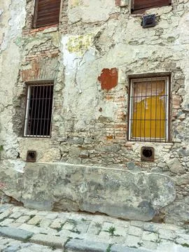 The wall shows wear with bricks exposed and broken windows with bars. A small Stock Photos