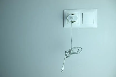 Wall socket with white cable on light wall Stock Photos