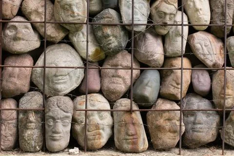 A wall of stones in the shape of human faces Stock Photos