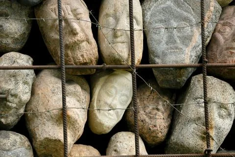 A wall of stones in the shape of human faces Stock Photos
