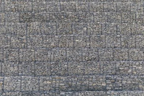 Wall texture assembled from blocks of river stones in a metal mesh Stock Photos