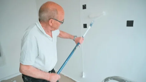 Walls gets painted with a paint roller by senior man working hard Stock Footage 107265287