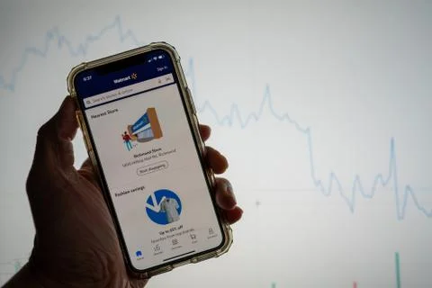 Walmart mobile app on iPhone in front of white stock market chart with graph Stock Photos