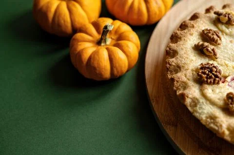 Walnut apple pie with small pumpkins on green background. Stock Photos