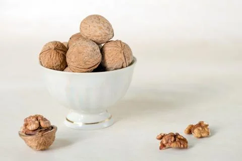 Walnut in a shell are stacked in a white cup. Next peeled nuts. Stock Photos