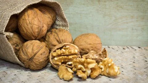 Walnut shells and walnut kernels bursting out of burlap sack on wicker surface. Stock Photos