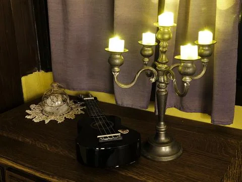 Walnut table with ukulele illuminated by a silver candlestick Stock Photos