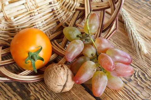 Walnut, tomato, grape and wheat ear over the wooden natural background. Stock Photos