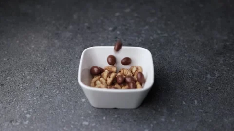 Walnuts and chocolate nuts falling into white bowl on gray background Stock Footage 320848053