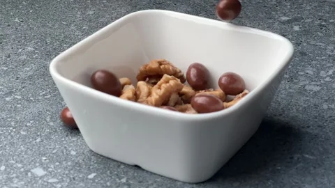 Walnuts and chocolate nuts falling together into small white bowl slow motion Stock Footage 321158110