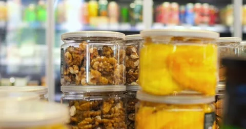 Walnuts and dried mango slices are displayed in clear jars on a supermarket Stock Footage 309047139