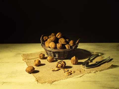 Walnuts in the basket in front of them broken walnut and nut tongs, dark back Stock Photos