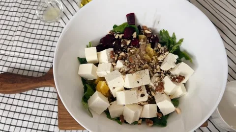 Walnuts fall as a sprinkle on a salad of fresh arugula with roasted beets, crumb Stock Footage 303051876