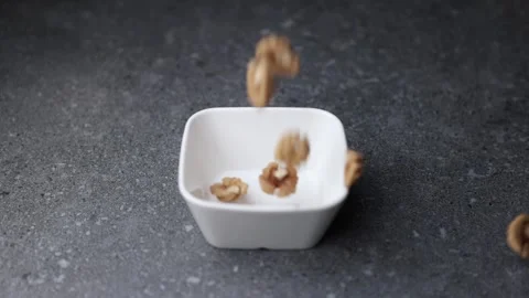 Walnuts falling into small white bowl on dark textured table surface Stock Footage 320848054