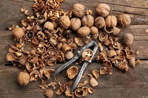 Walnuts, pieces of shells and nutcracker on wooden table, flat lay Stock Photos
