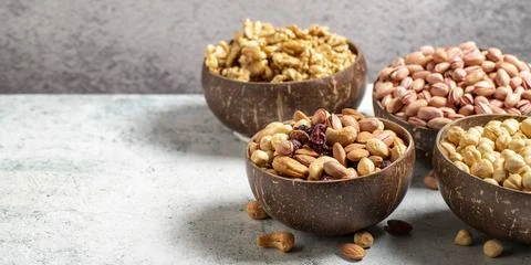 Walnuts, pistachios, hazelnuts and mixed nuts in a bowl on a gray background. Stock Photos