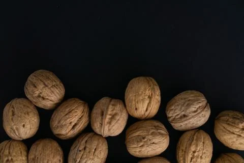 Walnuts in the shell on black surface, top view. Background of round walnuts Stock Photos