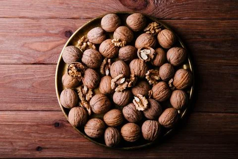 Walnuts in a shell in a golden plate on a brown background. Stock Photos