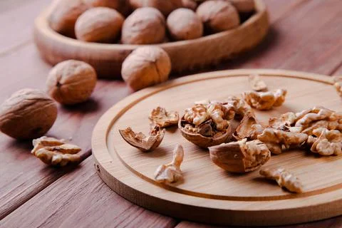 Walnuts in a shell in a wooden plate on a brown background. Stock Photos