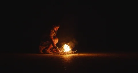 Wanderer with a beard sits by the fire and throws up wood at night Stock Footage 89827997