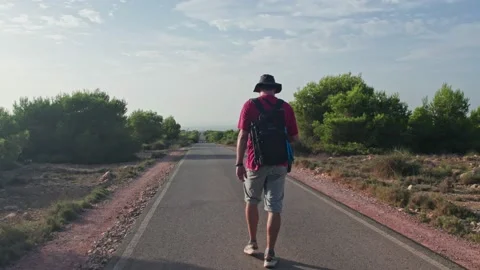 A wanderer in a cap with a backpack is walking along an asphalt, empty road.  Stock Footage 221913487