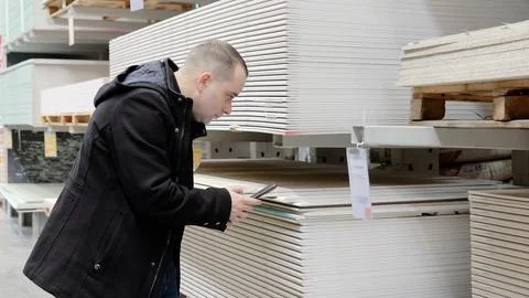 Warehouse customer comparing plasterboard prices on smartphone while walking Stock Photos