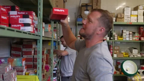 Warehouse employee organizing boxed hardware products on industrial shelving Stock Footage 331304771