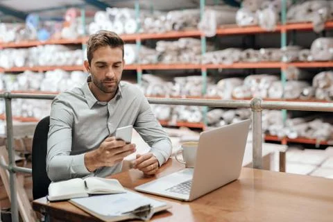 Warehouse manager checking his cellphone while working in his office Stock Photos
