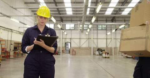 Warehouse manager works on a digital tablet while a worker shifts stock. Stock Footage 52668253