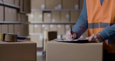 Warehouse operative preparing shipments and writing on a clipboard Stock Footage 297855997
