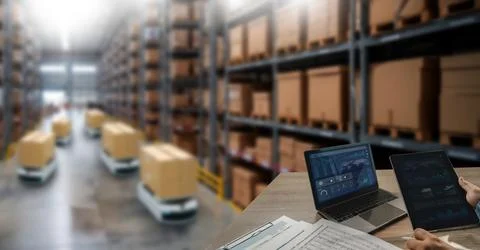 Warehouse robots transport boxes through storage aisles while a laptop and .. Stock Photos