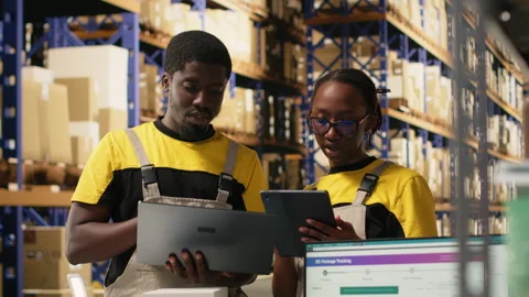 Warehouse staff overseeing parcels tracking info on laptop and tablet Stock Footage 315711240