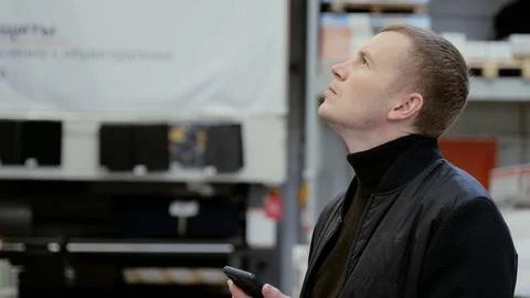 Warehouse supervisor is gazing at the ceiling while holding a smartphone, deep Stock Photos