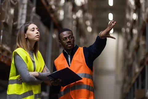 Warehouse supervisors discussing logistics operations while wearing high Stock Photos