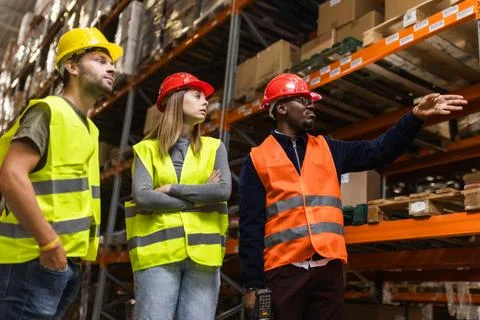 Warehouse team discussing logistics while wearing safety vests and helmets Stock Photos