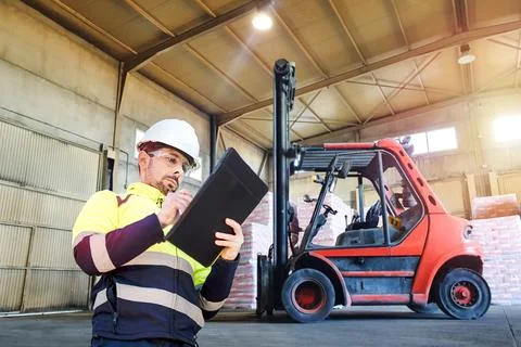 Warehouse Worker Checking Inventory Beside Forklift Stock Photos